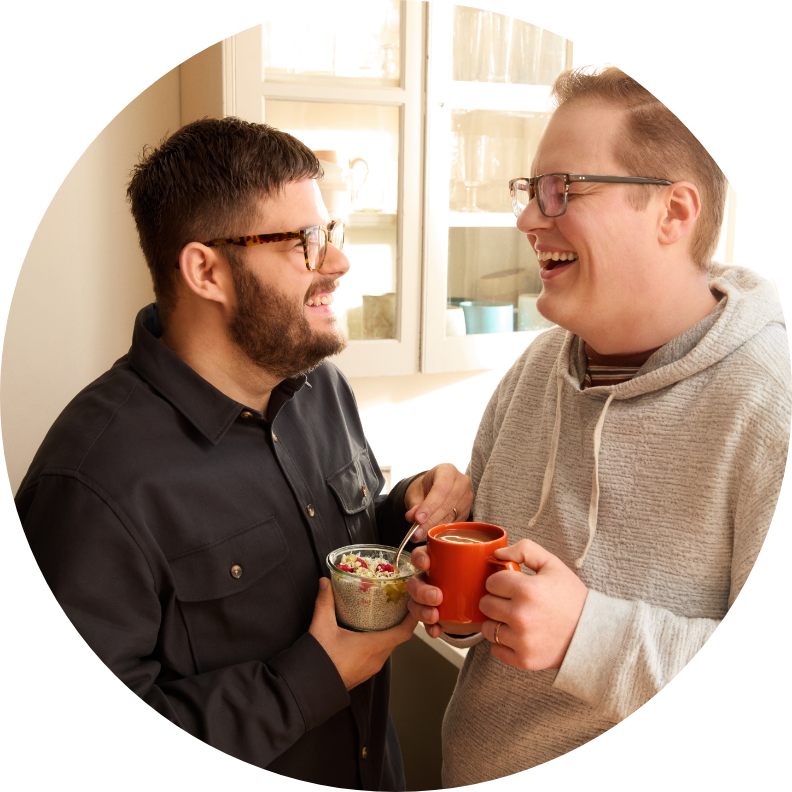 Two men smiling, looking forwards each other with a drink.